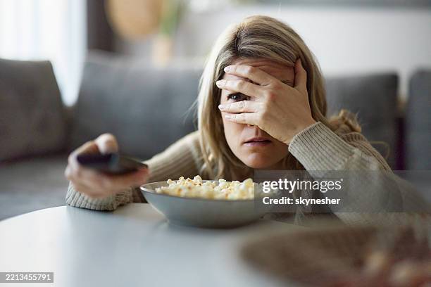 fearful woman watching tv in the living room. - part of a series stock pictures, royalty-free photos & images
