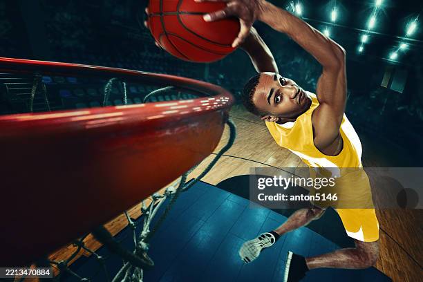 composite image. african american basketball athlete in yellow jersey executing powerful dunk. energetic movement frozen in time from wide angle on indoor court. - slam dunk stock pictures, royalty-free photos & images