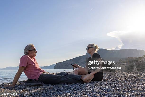 mature couple on beach with mobile phone at sunset - early retirement stock pictures, royalty-free photos & images
