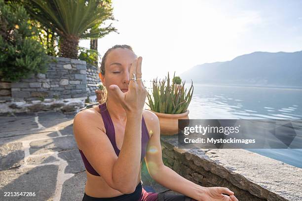 woman practicing breathing techniques by serene lake - pranayama stock pictures, royalty-free photos & images