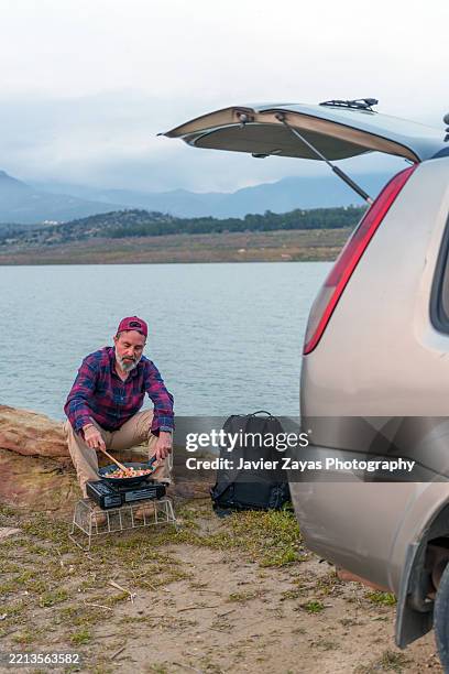 man cooking by lakeside with car nearby - car grill stock pictures, royalty-free photos & images