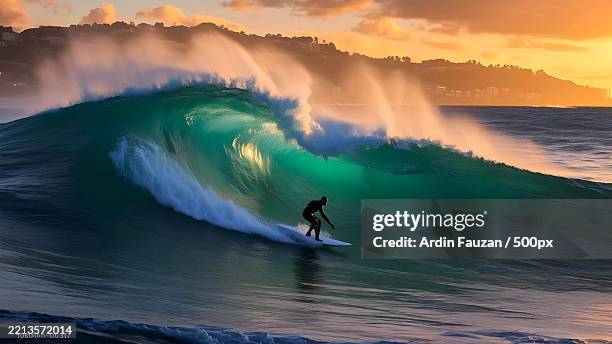 surfer riding a giant wave at sunset - surfer stock pictures, royalty-free photos & images