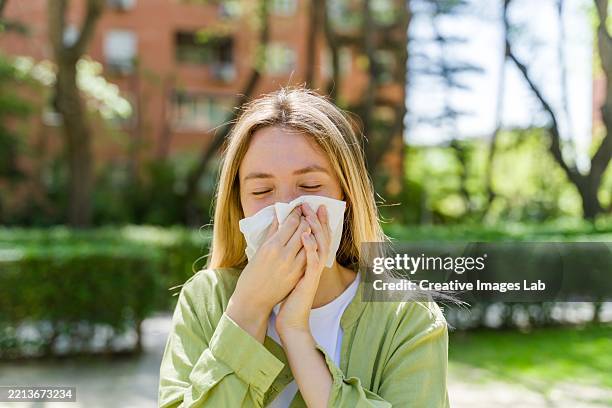 young woman sneezing due to spring allergies - sneeze stockfoto's en -beelden
