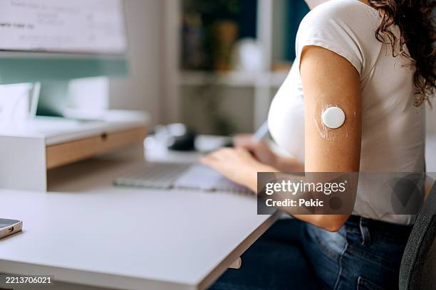 close up shot of young woman working from home with diabetes sensor on arm - glucose stockfoto's en -beelden