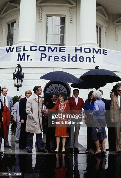 President Ronald Reagan and First Lady Nancy Reagan standing under umbrellas at the White House in Washington, April 12th 1981. They are joined by...