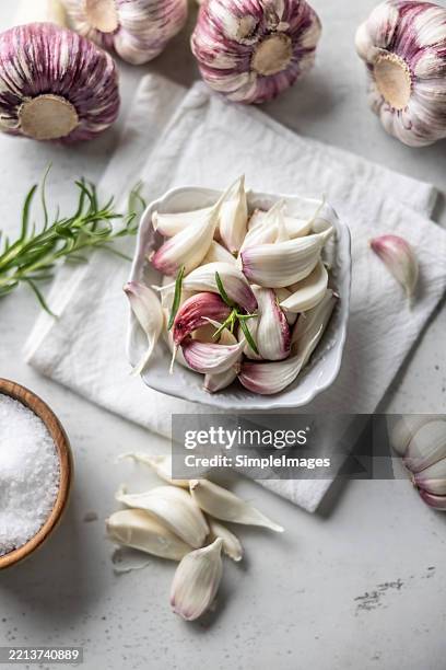 a pile of garlic cloves in a bowl on a rustic white towel with rosemary - garlic stock pictures, royalty-free photos & images