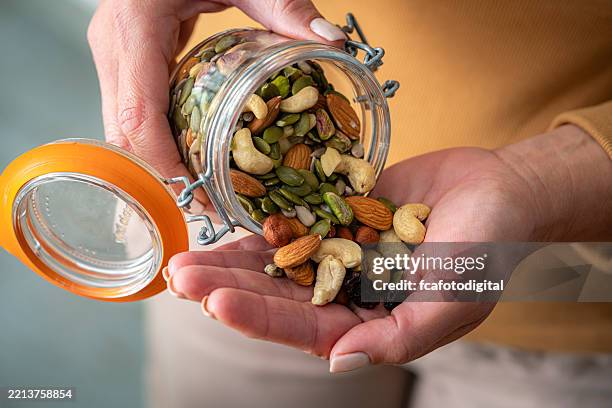 primo piano delle mani della donna che versano noci e semi dal contenitore al palmo della mano - mischiare foto e immagini stock