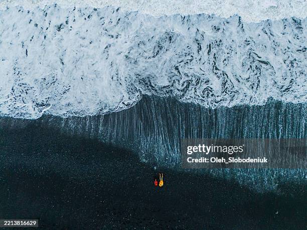 aerial view of man and woman walking on black sand beach in iceland - honra imagens e fotografias de stock