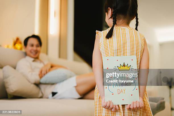 asian little girl hiding a father's day greeting card at back and walking to her father - fathers day stock pictures, royalty-free photos & images
