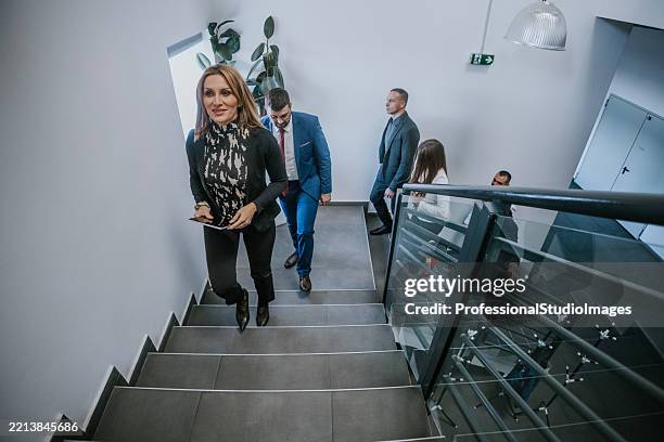 group of professionals walking up a staircase in a modern office environment - balustrade stock pictures, royalty-free photos & images