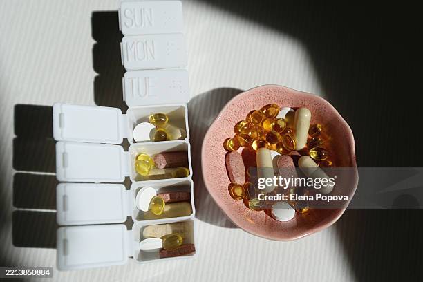 open individual pillbox with heap of small vitamin d capsules and mineral pills next the pink ceramic bowl full of nutritional supplements - hormone stock pictures, royalty-free photos & images