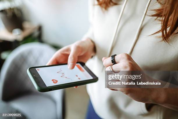 woman in a hoodie with a smart ring checks heart rate on her phone app - application mobile photos et images de collection