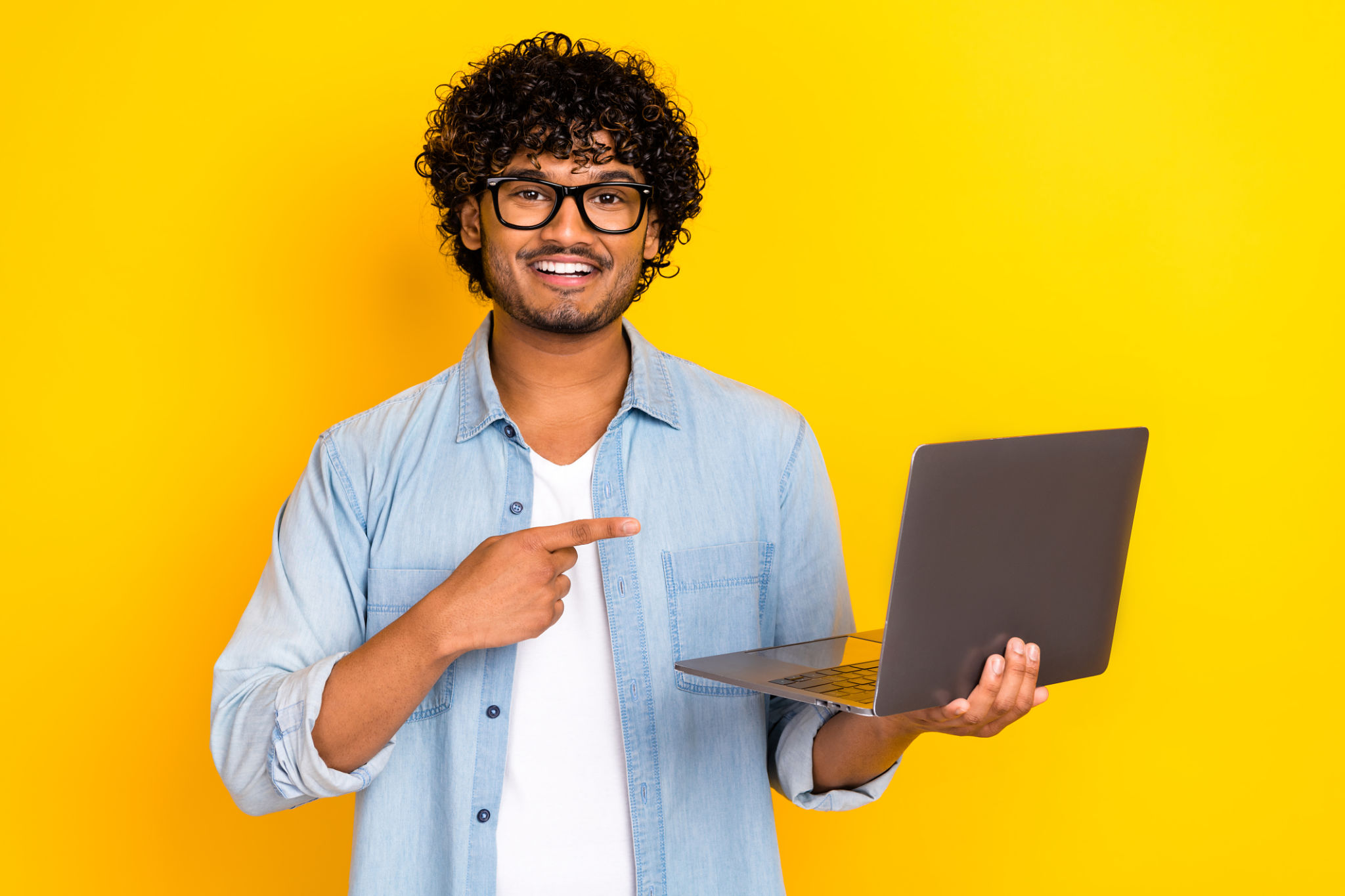 Foto de um cara bonito e alegre indica o netbook microsoft da maçã do dedo isolado no fundo de cor amarela Foto de um cara bonito e alegre indica o netbook microsoft da maçã do dedo isolado no fundo de cor amarela