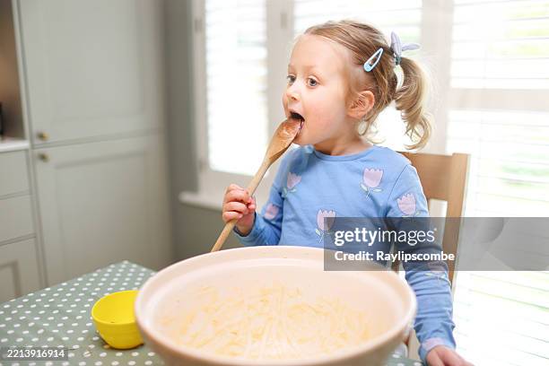 vierjähriges mädchen kratzt und isst mit einem holzlöffel die letzten reste einer biskuitmasse aus einer großen keramikrührschüssel - kuchenteig stock-fotos und bilder