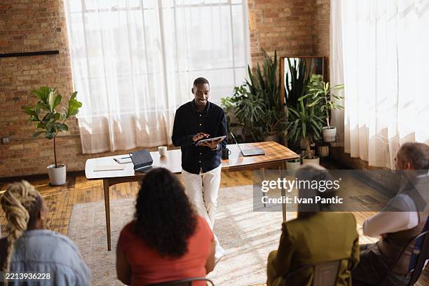 confident young businessman leading a team meeting in a modern office space - sales executive stock pictures, royalty-free photos & images