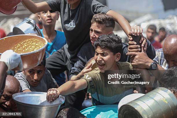 Palestinians wait to receive a hot meal at a food distribution centre as food crisis and humanitarian situation worsen amid the ongoing Israeli...