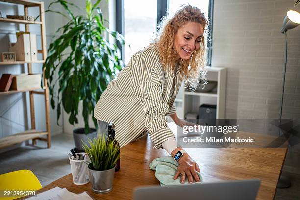 smiling woman cleaning desk in home office - housework stock pictures, royalty-free photos & images