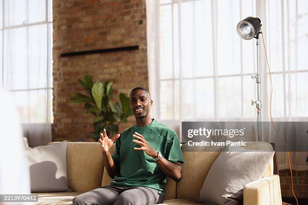 young man recording a video interview sitting on a sofa - theaterdecor stockfoto's en -beelden