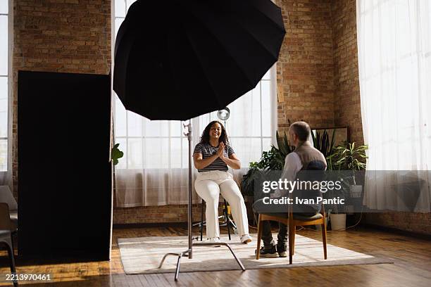 photographer taking pictures of a smiling model during a photoshoot in a loft studio - media interview stock pictures, royalty-free photos & images