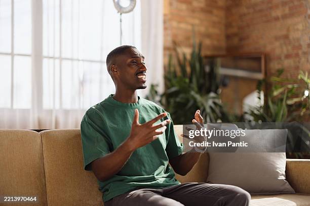 young man having a conversation sitting on a sofa at home - entrevista dos meios de comunicação social imagens e fotografias de stock