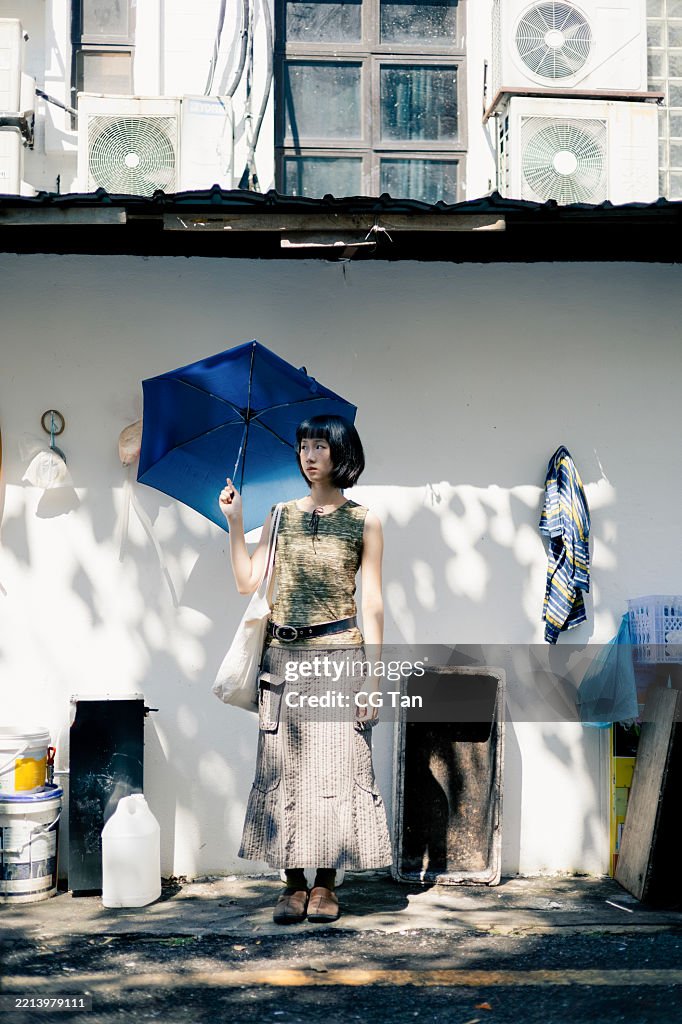 Young Asian Chinese Woman Standing with Blue Umbrella Against white Wall