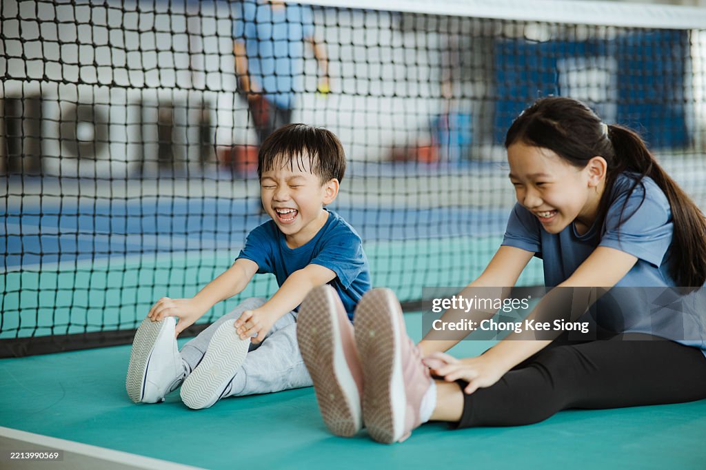 Dos niños asiáticos de último año estirándose antes de jugar pickleball.