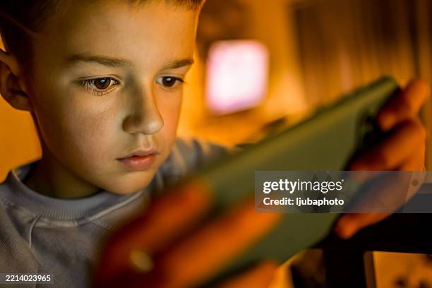 young boy focused on a mobile device in warm lighting - staring at screen stock pictures, royalty-free photos & images