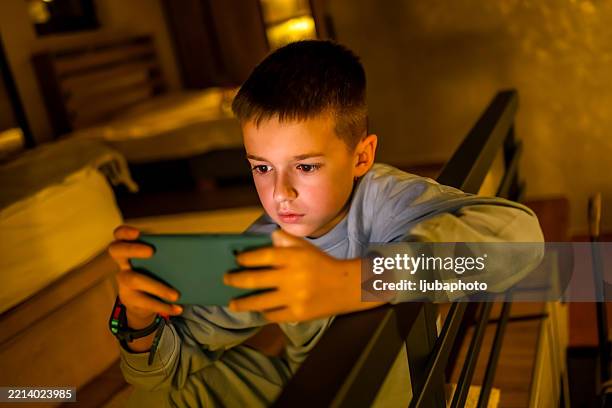 young boy playing mobile game on smartphone in a cozy home setting - gameplay stock pictures, royalty-free photos & images
