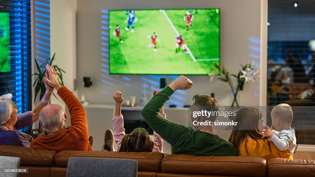 Famille multigénérationnelle excitée regardant un match de football dans un salon confortable
