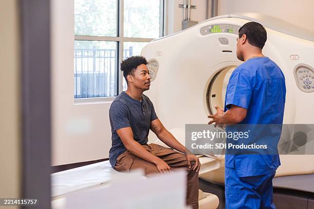 young man and doctor discussing ct scan procedure - tomography stock pictures, royalty-free photos & images