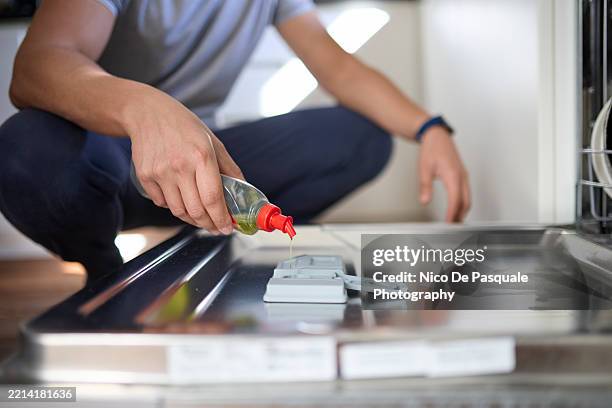 man pouring rinse aid into dishwasher dispenser at home - spülmittel stock-fotos und bilder