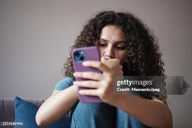 worried anxious gen z girl looking at smartphone screen feeling upset scrolling on social media. doomscrolling and mental health. sad girl using mobile phone biting nails - nail biting stock pictures, royalty-free photos & images