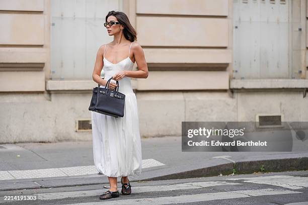 Katie Degas @katie.one wears a white bustier-style bubble midi dress with thin spaghetti straps and a voluminous balloon hem by Shona Joy. Black...