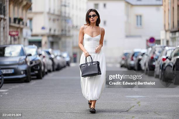 Katie Degas @katie.one wears a white bustier-style bubble midi dress with thin spaghetti straps and a voluminous balloon hem by Shona Joy. Black...