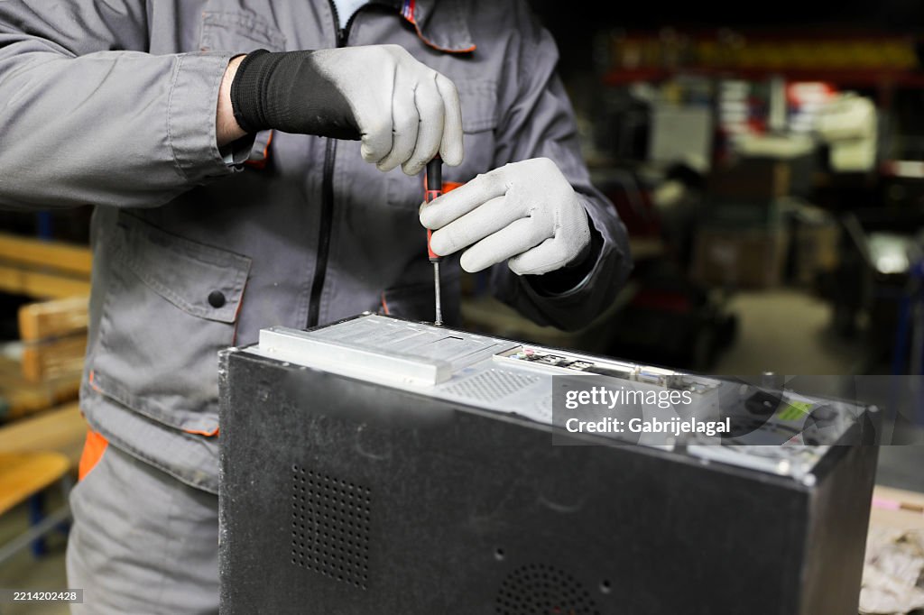 Gray-haired technician using compressed air to clean dusty computer parts.