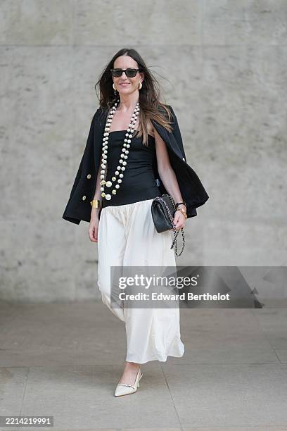 Alba Garavito Torre wears long straight brown hair parted slightly off-center. A tailored black double-breasted blazer with gold buttons by Sandro is...