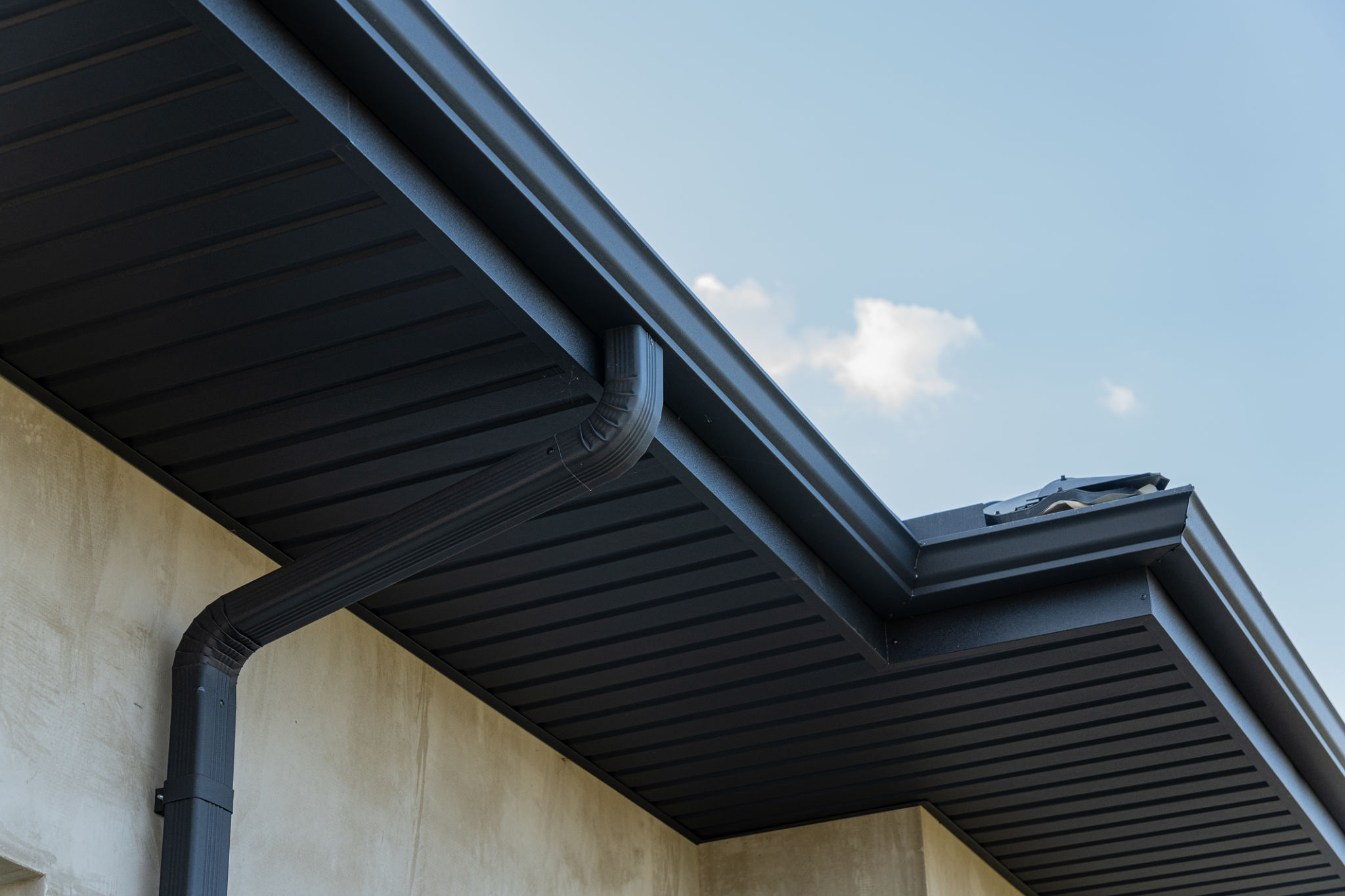 Exterior view of a contemporary home highlighting a sleek black gutter along the roofline under a bright blue sky Exterior view of a contemporary home highlighting a sleek black gutter along the roofline under a bright blue sky