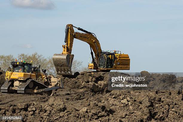 a large yellow caterpillar excavator and bulldozer work together on a rugged, muddy construction site - construction equipment stock pictures, royalty-free photos & images