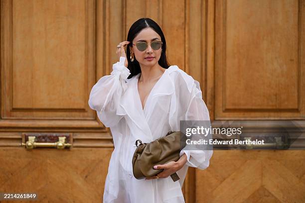 Patricia Gloria Contreras wears wears long, straight black hair with a middle part, dark lipstick and defined brows. Gold angular sunglasses are...