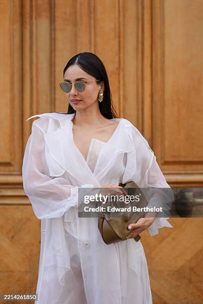 Patricia Gloria Contreras wears wears long, straight black hair with a middle part, dark lipstick and defined brows. Gold angular sunglasses are...