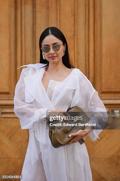 Patricia Gloria Contreras wears wears long, straight black hair with a middle part, dark lipstick and defined brows. Gold angular sunglasses are...