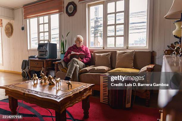 älterer mann, der sich zu hause entspannt und in seinem wohnzimmer ein buch liest - einzelner senior stock-fotos und bilder