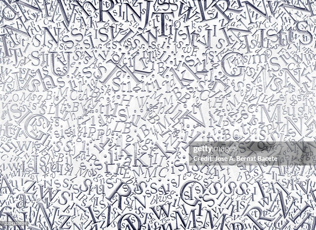 Abstract background, jumbled alphabet letters in metallic silver tones on a white background.