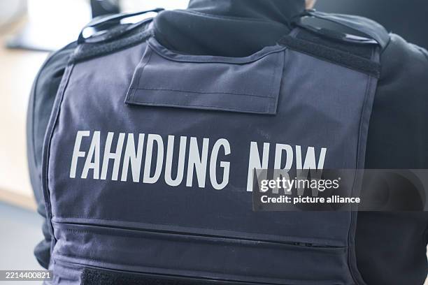May 2025, North Rhine-Westphalia, Duesseldorf: ILLUSTRATION - An employee wearing a protective vest bearing the inscription "Fahndung NRW" sits at a...