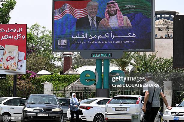 People walk past a billboard displaying portraits of Saudi Crown Prince Mohammed bin Salman and US President Donald Trump with a slogan thanking...