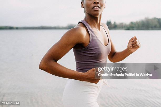 midsection of a woman jogging by a tranquil body of water - thin stock pictures, royalty-free photos & images