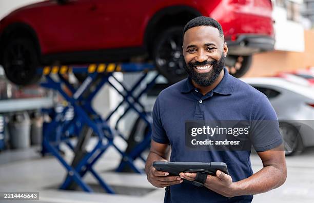 mechaniker, der in einer autowerkstatt arbeitet und ein digitales tablet in der hand hält - automechaniker stock-fotos und bilder