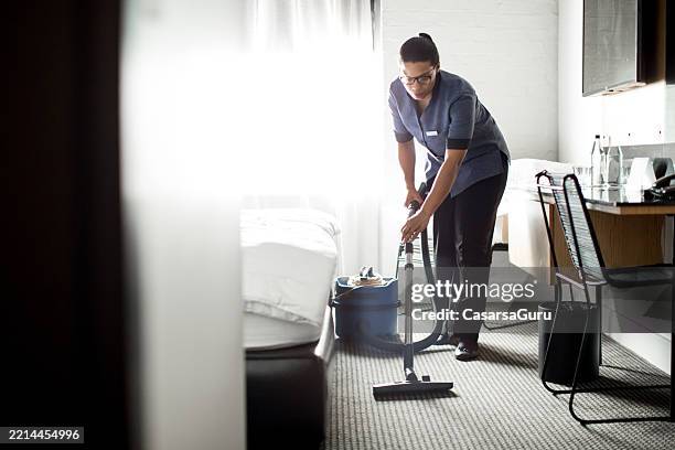 femme de ménage passant l’aspirateur sur le tapis dans une chambre d’hôtel - agent de ménage photos et images de collection