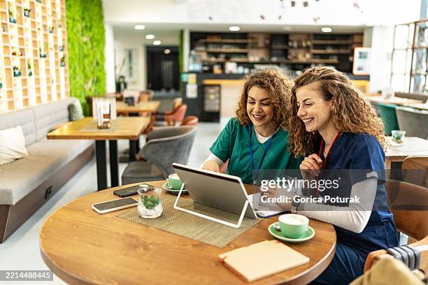two nurses laughing while looking at tablet in cafe - nurses laughing stock pictures, royalty-free photos & images