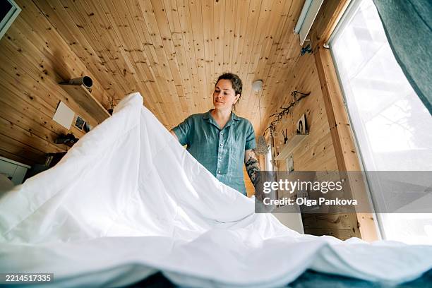 woman making bed in cozy wooden tiny house - bettbezug stock-fotos und bilder